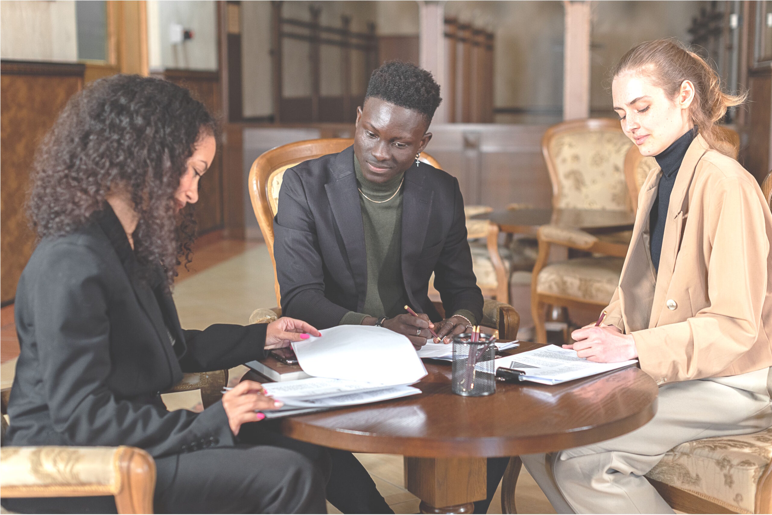 Three people reviewing papers together at a round wooden table